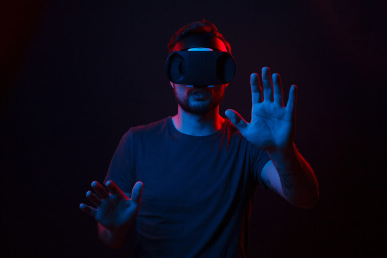 Man wearing a VR headset experiencing virtual reality, with hands outstretched in a dark room with blue and red lighting.