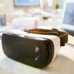 A VR headset on a modern desk, next to a laptop displaying financial charts and data.
